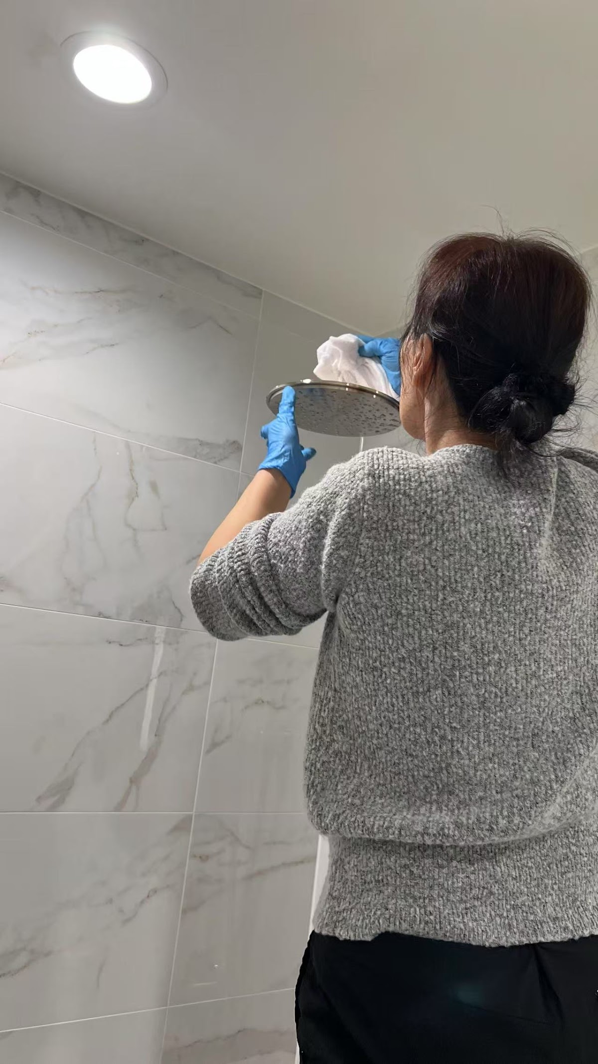 Cleaner wiping bathroom wall tiles wearing protective gloves
